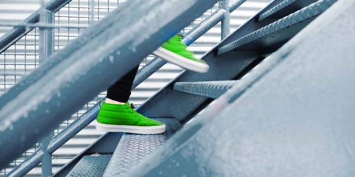 Sinnbild für Aufstieg und unternehmerischen Erfolg. Das Bild zeigt zwei Schuhe auf einer Treppe, gerade in der Bewegung eine Stufe nach oben zu gehen. Der Blickwinkel ist besonders, denn der Betrachter schaut zwischen den Streben des Treppengeländers hindurch. Diese ungewöhnliche Perspektive steht sinnbildlich für den Perspektivwechsel, den es manchmal benötigt, um als Unternehmen von neuen Denkansätzen zu profitieren.